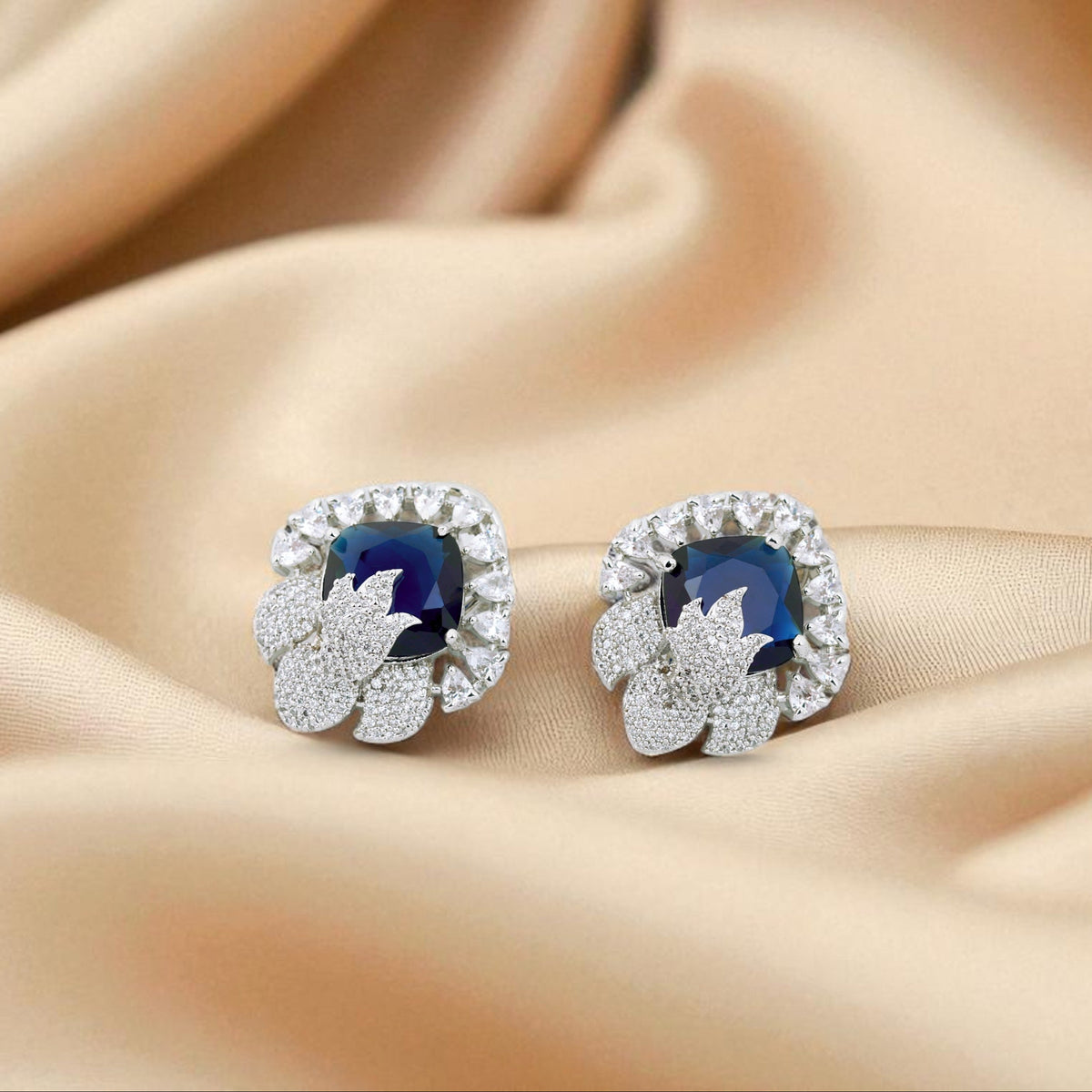 Pair of silver earrings with blue gemstones on a beige fabric background