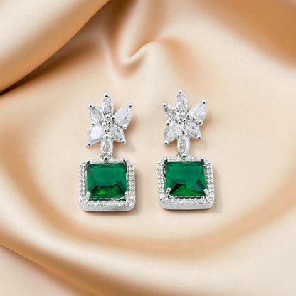 Green gemstone earrings with silver accents on a beige fabric background