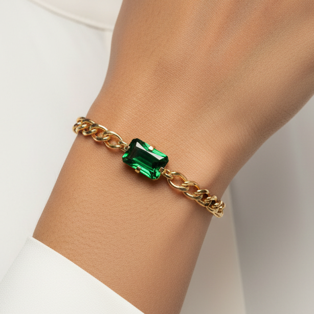 Gold bracelet with a green gemstone on a person's wrist against a white background