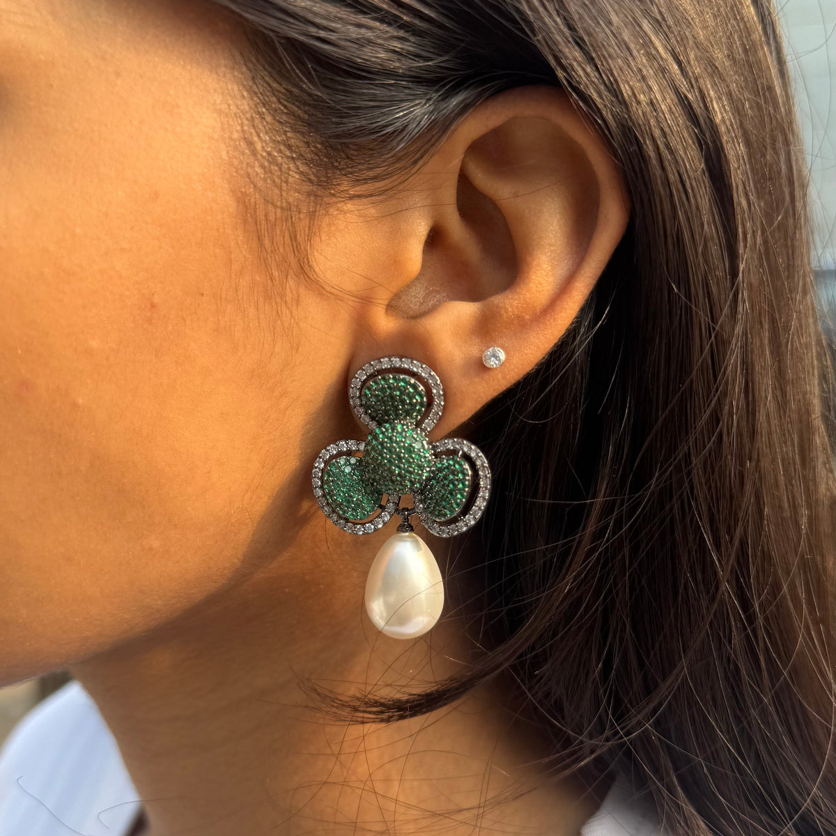 Close-up of a person wearing a green and white floral earring with a pearl accent.