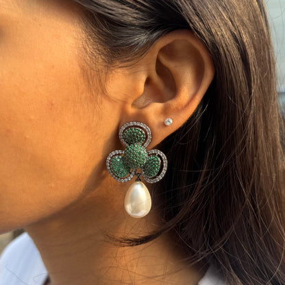 Close-up of a person wearing a green and white floral earring with a pearl accent.