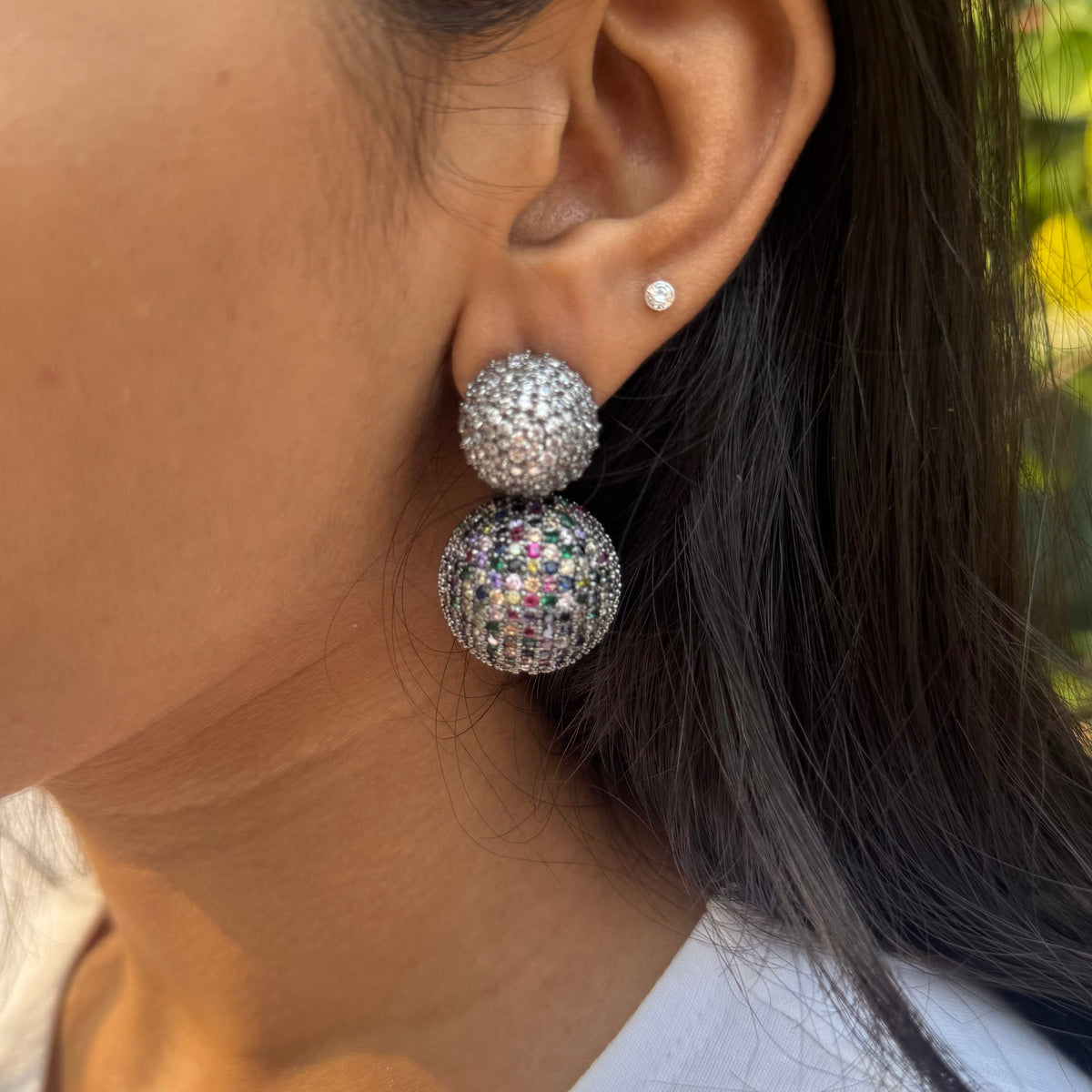 Close-up of a person wearing sparkling silver earrings outdoors.