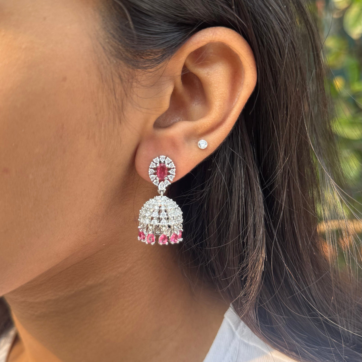 Close-up of a person wearing red and silver earrings outdoors.