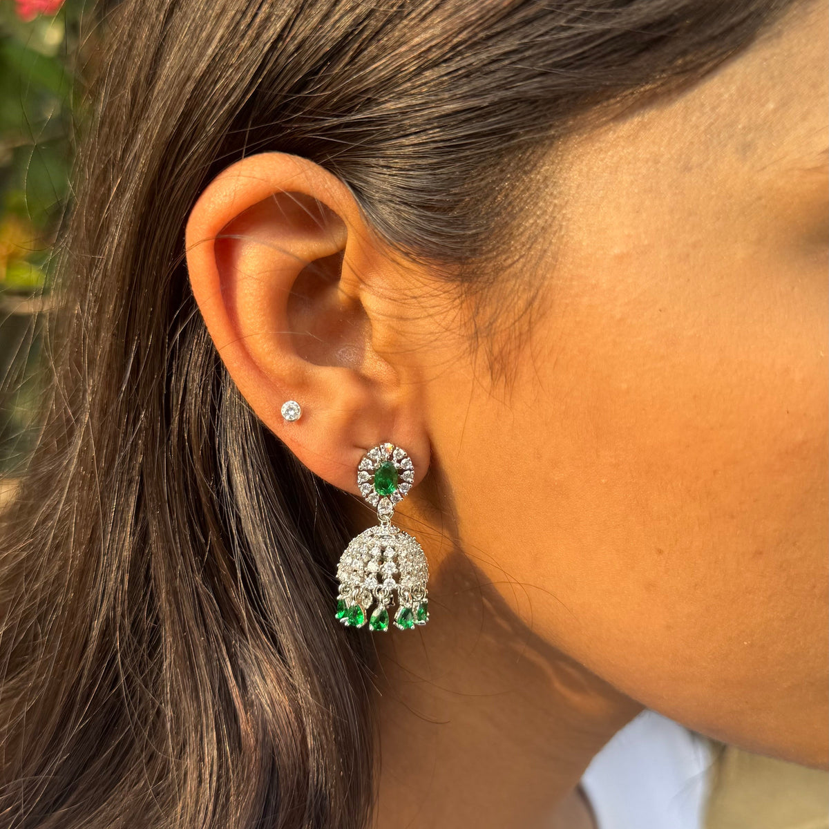 Close-up of a person wearing a green and silver earring with a blurred background