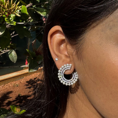 Close-up of a person wearing a silver hoop earring with a blurred green outdoor background