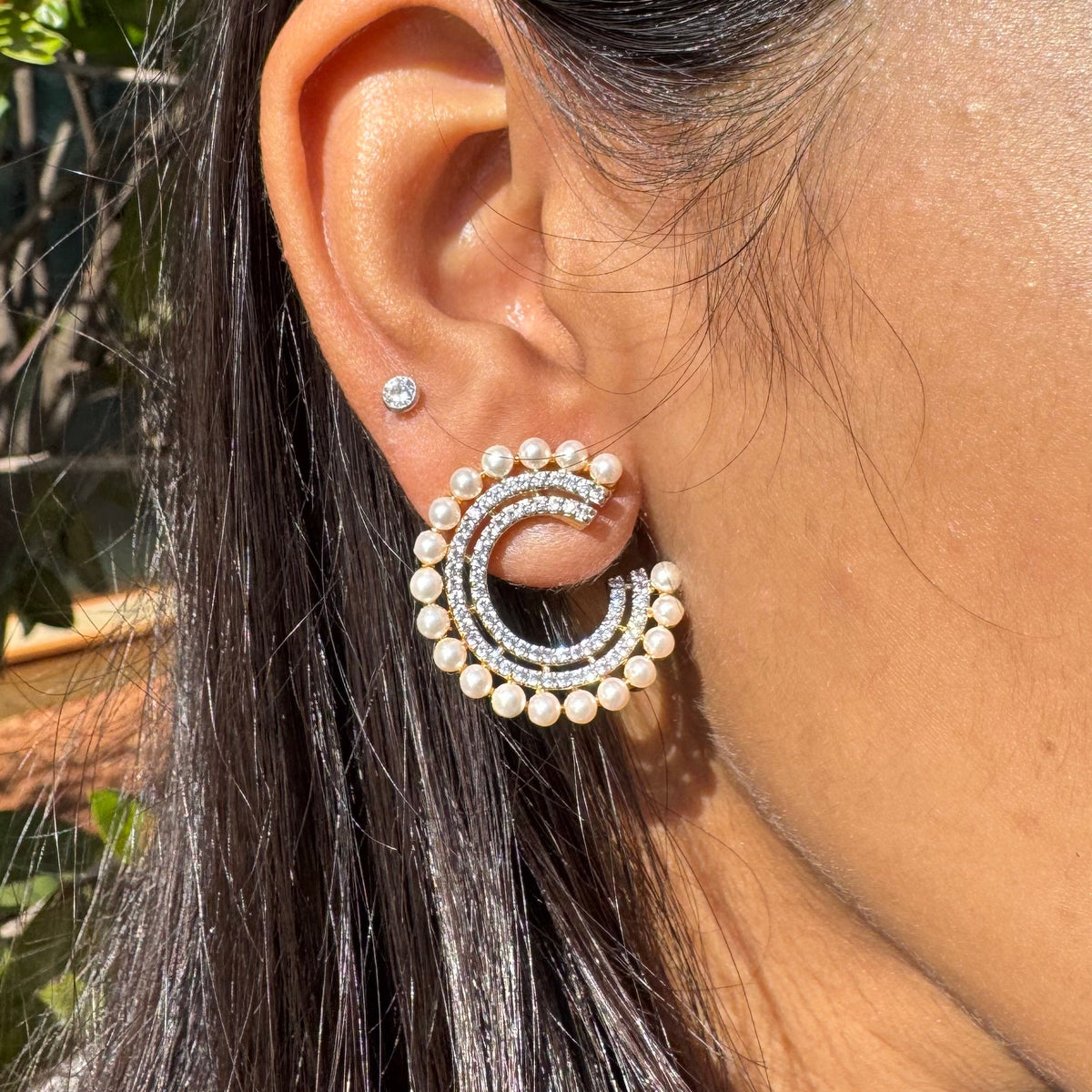 Close-up of an ear wearing a pearl earring with a blurred natural background