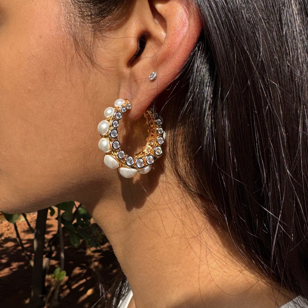 Close-up of an ear wearing a gold hoop earring with pearls and a small diamond.