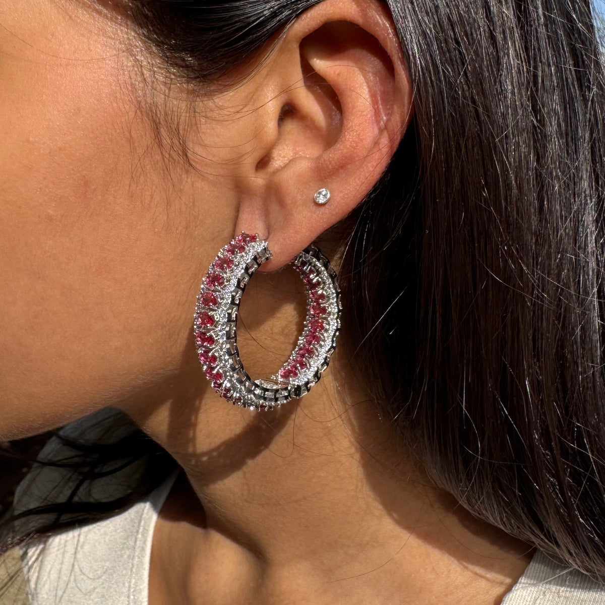 Close-up of a person wearing a silver hoop earring with pink gemstones.