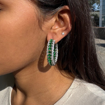 Close-up of a person wearing green hoop earrings with a blurred outdoor background