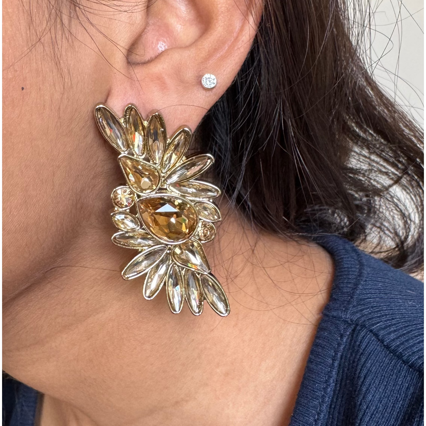 Close-up of a person wearing a large, ornate earring with a neutral background