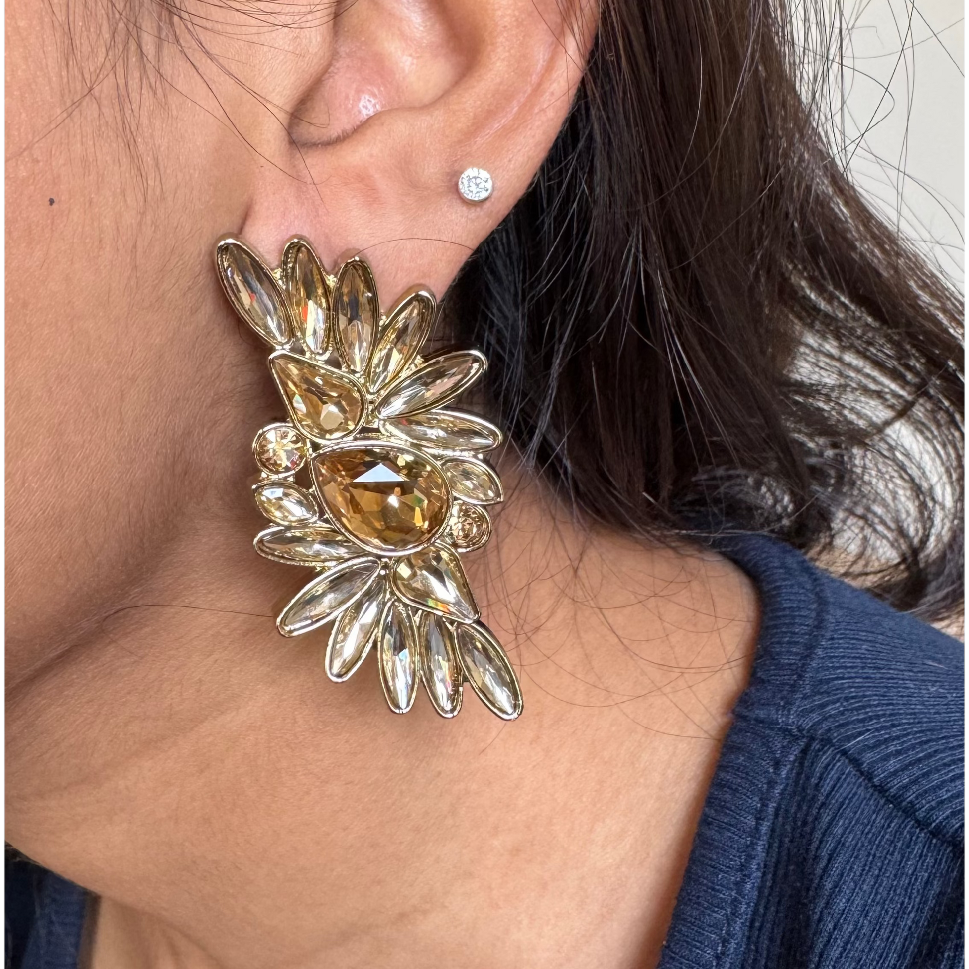 Close-up of a person wearing a large, ornate earring with a neutral background