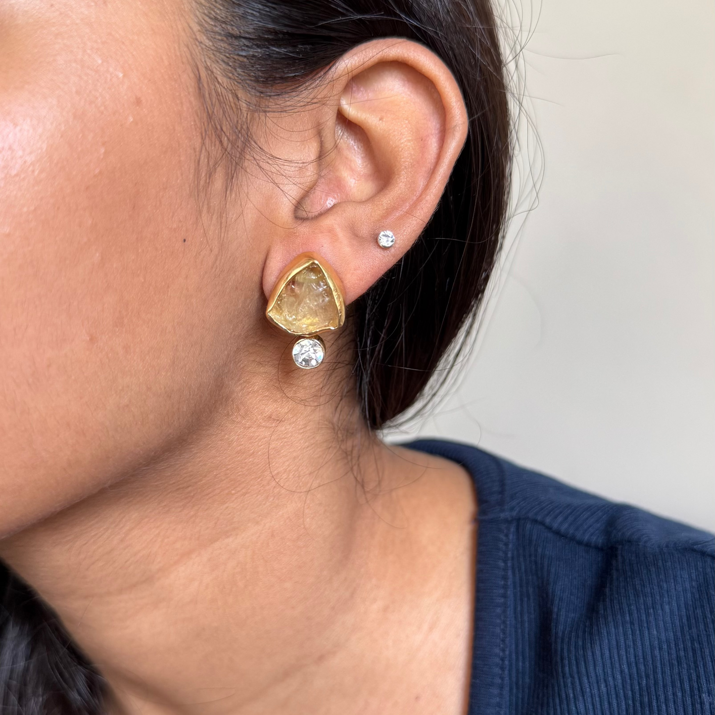 Close-up of a person wearing gold triangle earrings with clear stones.