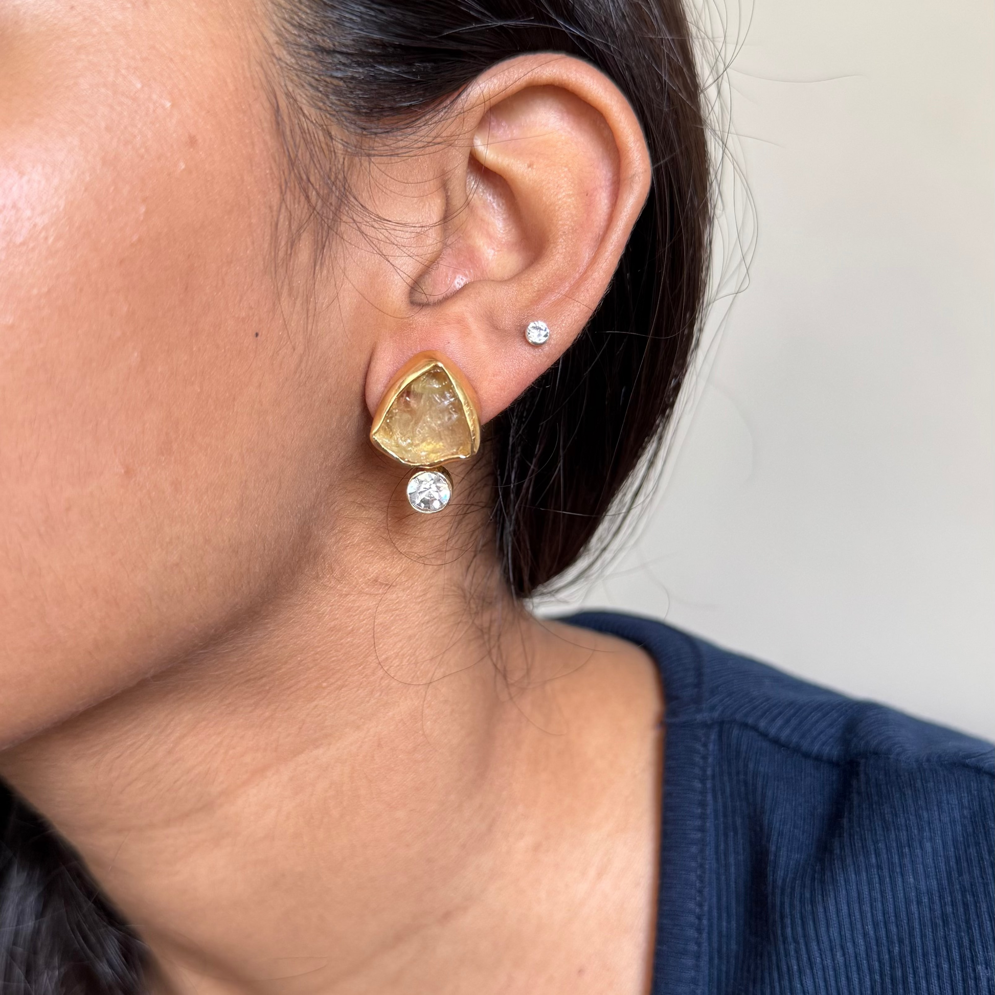 Close-up of a person wearing gold triangle earrings with clear stones.