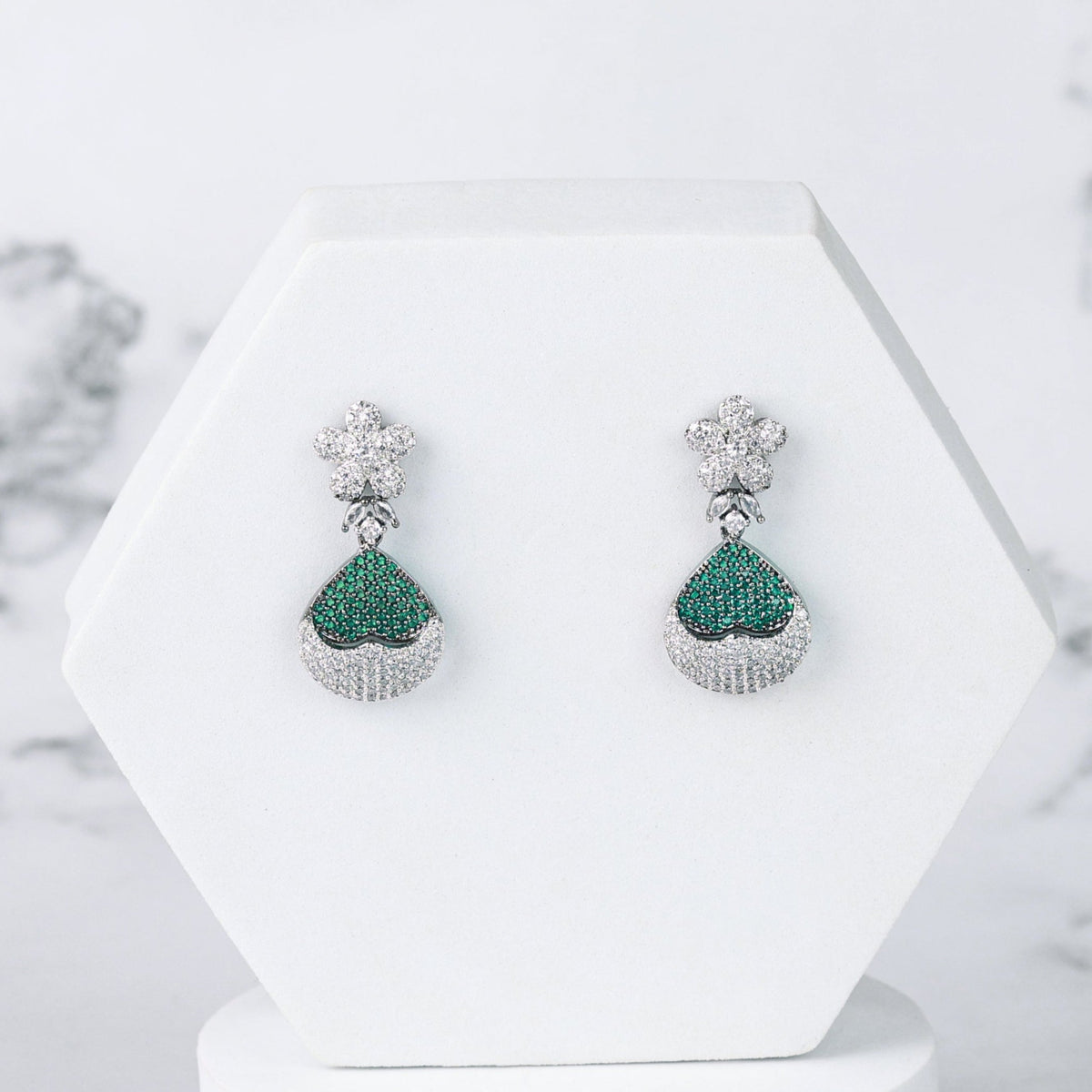 Pair of green diamond earrings on a white stand with a marble background